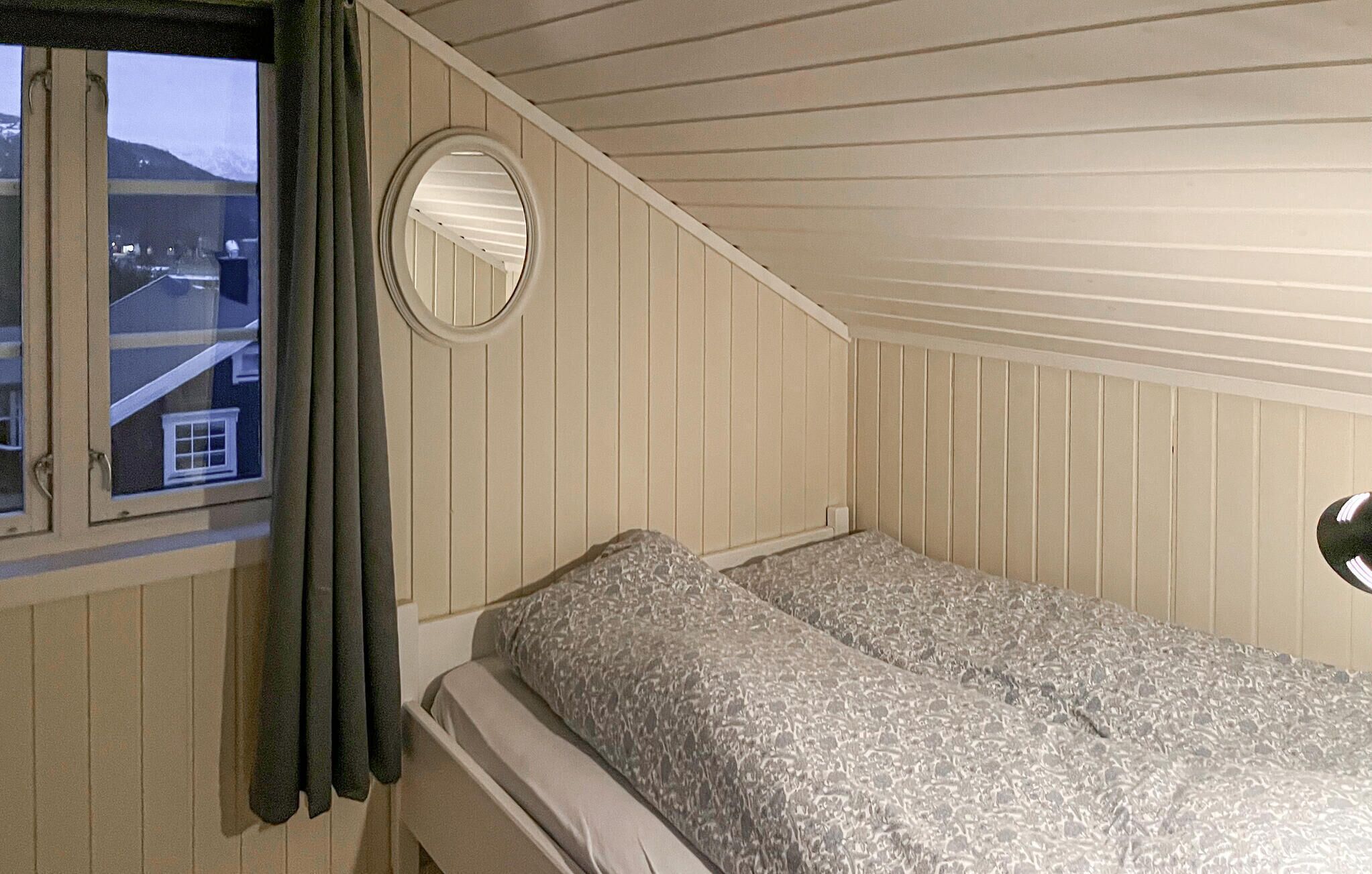 Une chambre avec une fenêtre, un miroir rond et un lit avec une literie à motifs.