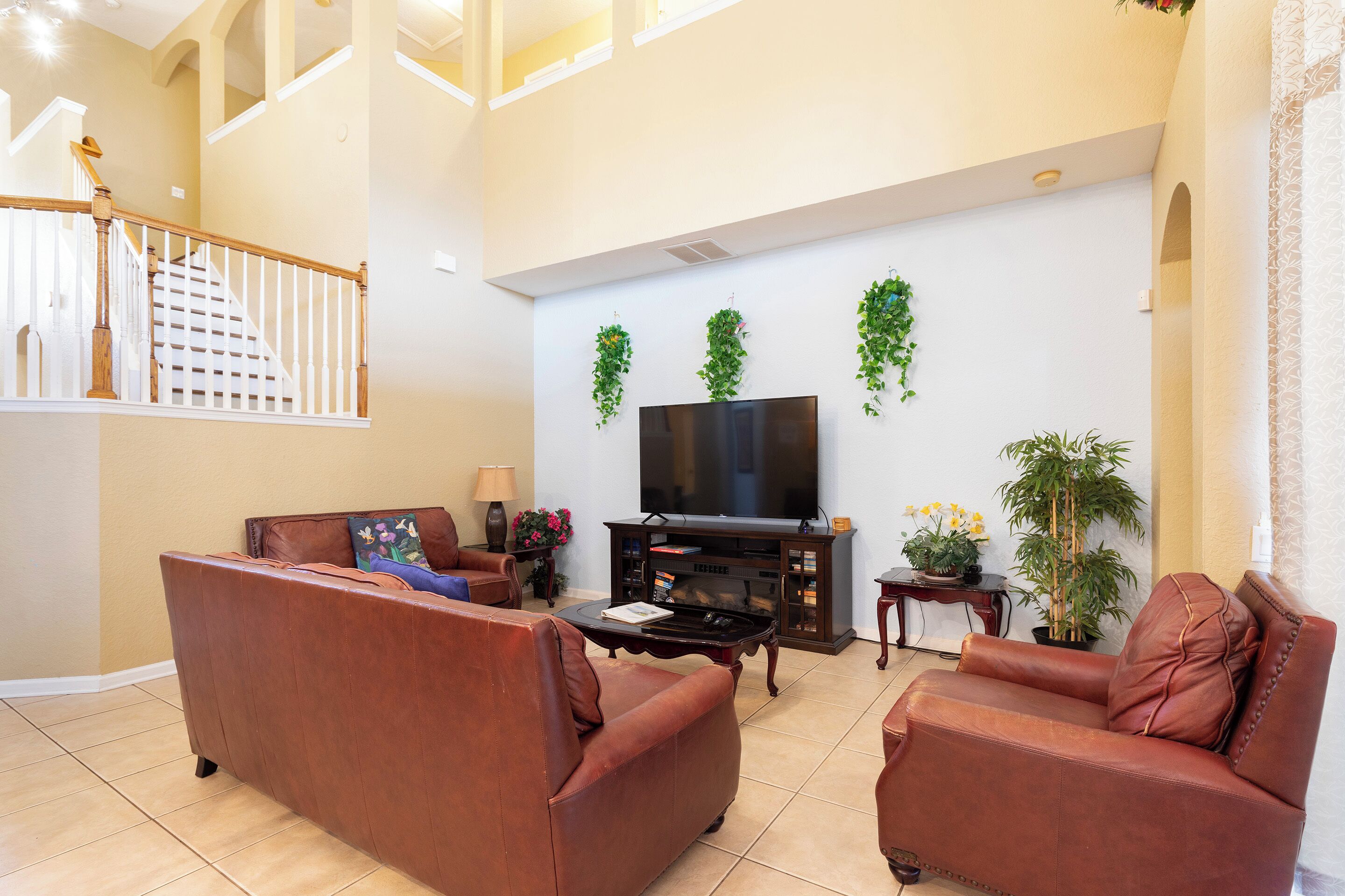A spacious living room with a brown leather sofa, a flat-screen TV, and a staircase leading to an upper level.