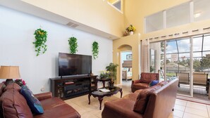 A living room with a flat-screen TV, leather sofas, a coffee table, and potted plants. - Windsor Hills Resort (Kissimmee)