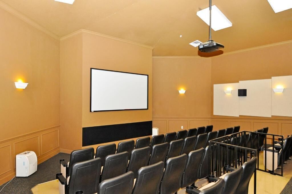 A conference room with rows of chairs, a projector screen, and wall-mounted screens.