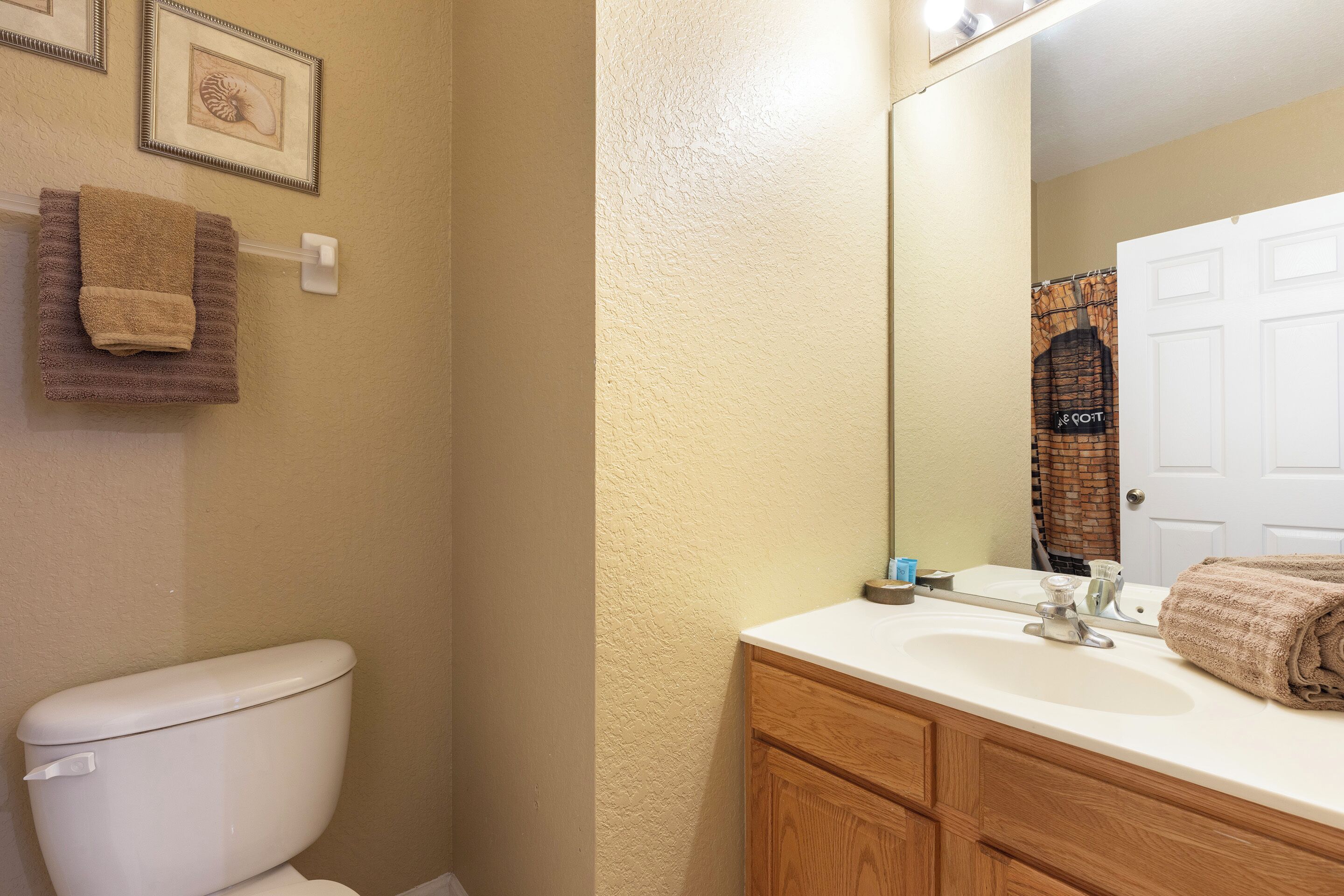 A bathroom with a white toilet, a sink with a mirror, and a towel hanging on the wall.