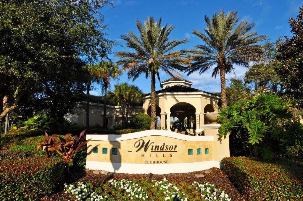A sign for Windsor Hills Clubhouse surrounded by lush greenery and palm trees.