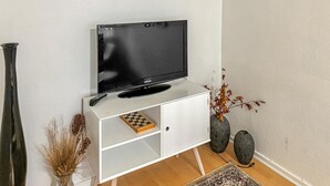 A white TV stand with a Samsung TV, a remote, a chessboard, and decorative vases. - Nice apartment in Esbjerg with WiFi (Esbjerg)