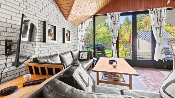 A modern living room with a brick wall, leather sofa, wooden table, and a view of the outdoors. - 3 bedroom amazing home in Nørre Nebel (Nørre Nebel)