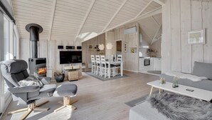 Een ruime woonkamer met een open haard, een eettafel en een keuken op de achtergrond.