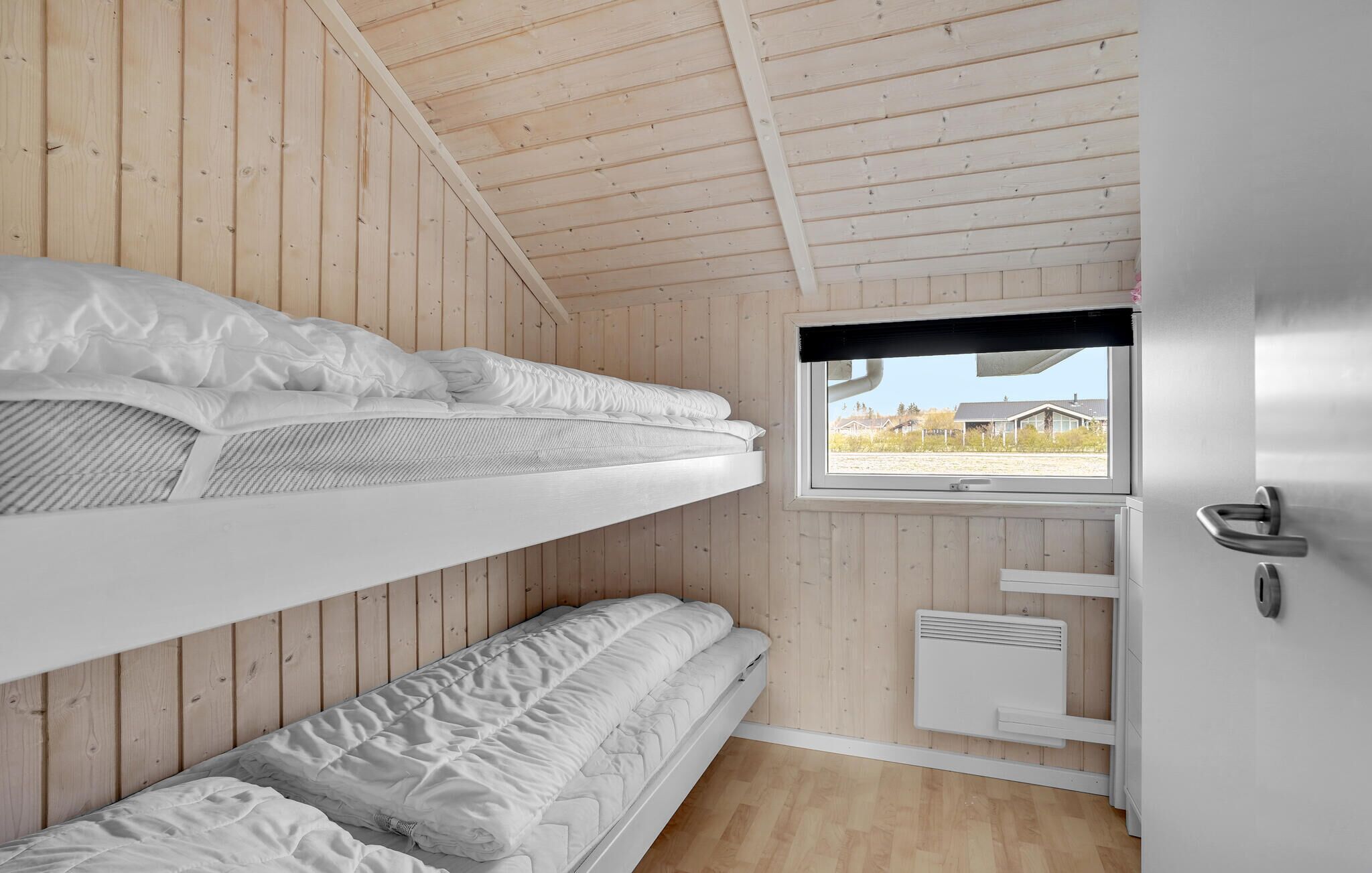 A bunk bed room with wooden walls, a window with a view, and a white door.