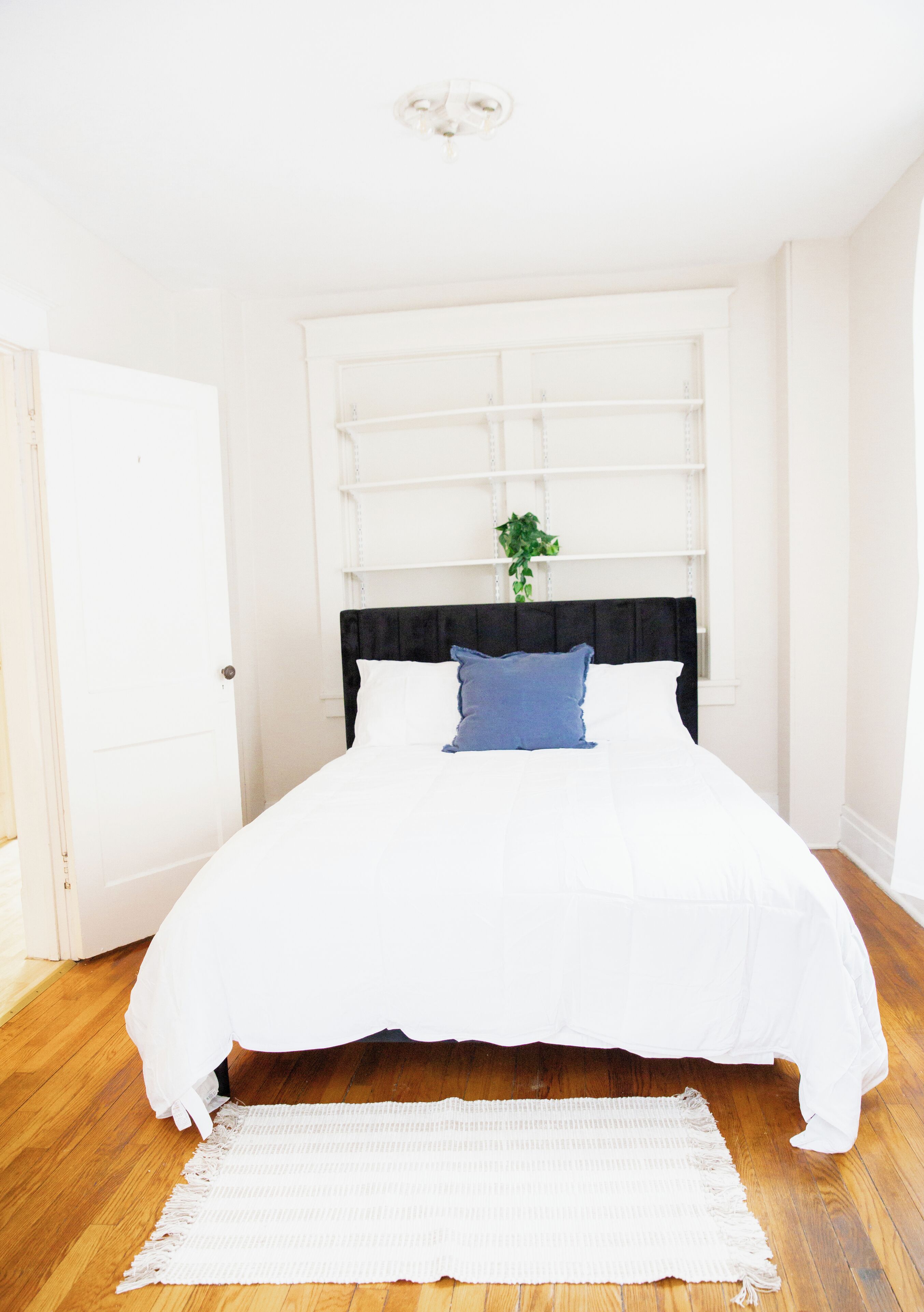 Una cama con cabecera negra, ropa de cama blanca y almohada azul.