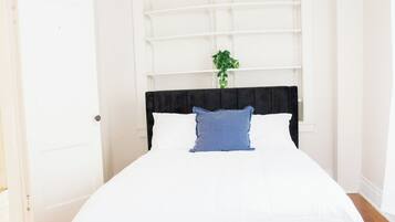 Una cama con cabecera negra, ropa de cama blanca y almohada azul.