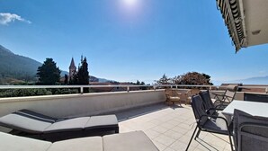 A rooftop terrace with lounge chairs, a table, and a view of a church and mountains. - Apartment Rilić by Interhome (Zaostrog)