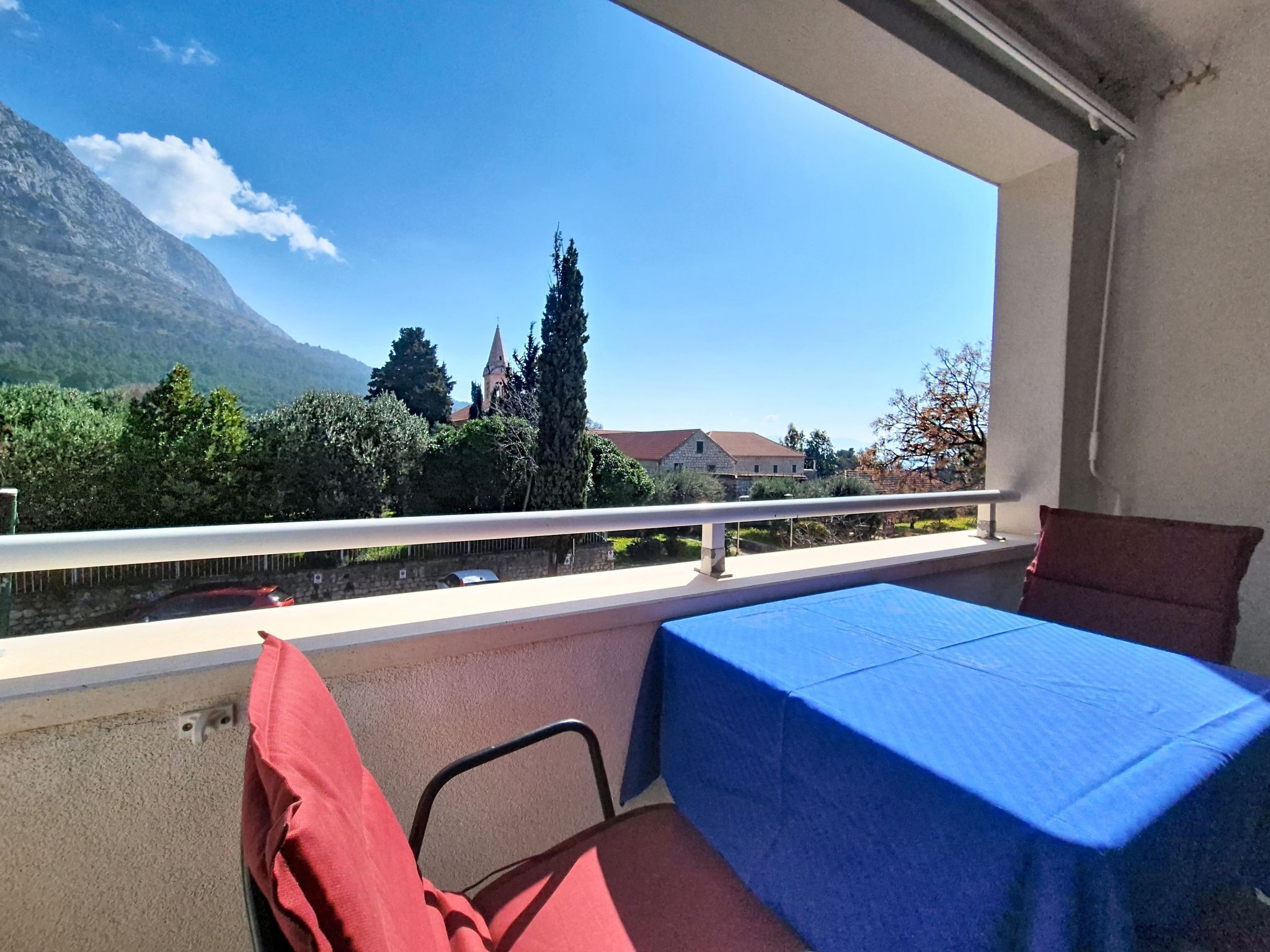 A balcony with a table and chairs, a view of a mountain, and a building with a tower.