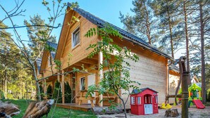 Una cabana de fusta amb un porxo, envoltada d'arbres i un parc infantil.
