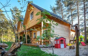 A wooden cabin with a porch, surrounded by trees and a playground. - 2 bedroom amazing home in Pobierowo (Pobierowo)
