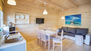Interior acollidor d'una cabana amb zona de dinar, un sofà, una televisió i un quadre amb una escena de platja.