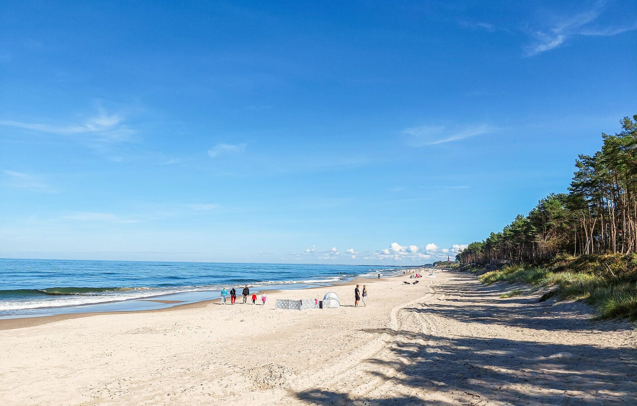 A sandy beach with a clear blue sky, a few people walking, and a tent set up.