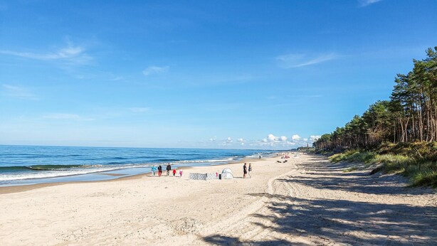 En sandstrand med en klarblå himmel, några få personer som promenerar och ett tält som är uppsatt.