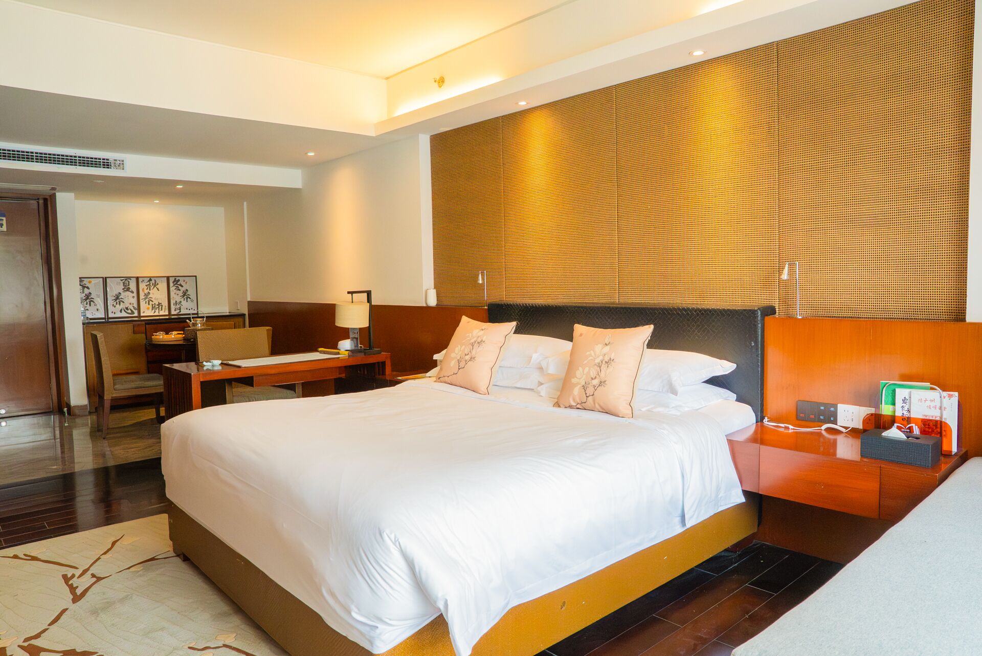 A hotel room with a large bed, a desk, a chair, a nightstand, and a wall with a textured pattern.