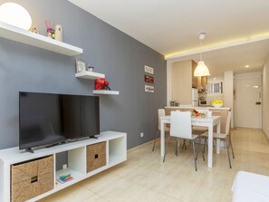 A modern living room with a flat-screen TV, white furniture, and a dining area with a table and chairs. - Apartment Gudrum by Interhome (La Pineda)