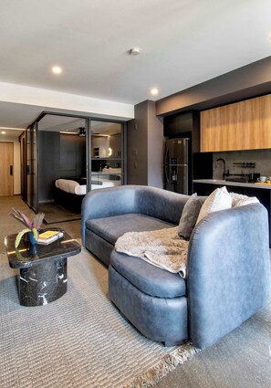 Ein modernes Wohnzimmer mit einem grauen Sofa, einem kleinen schwarzen Beistelltisch und einer Küche im Hintergrund.