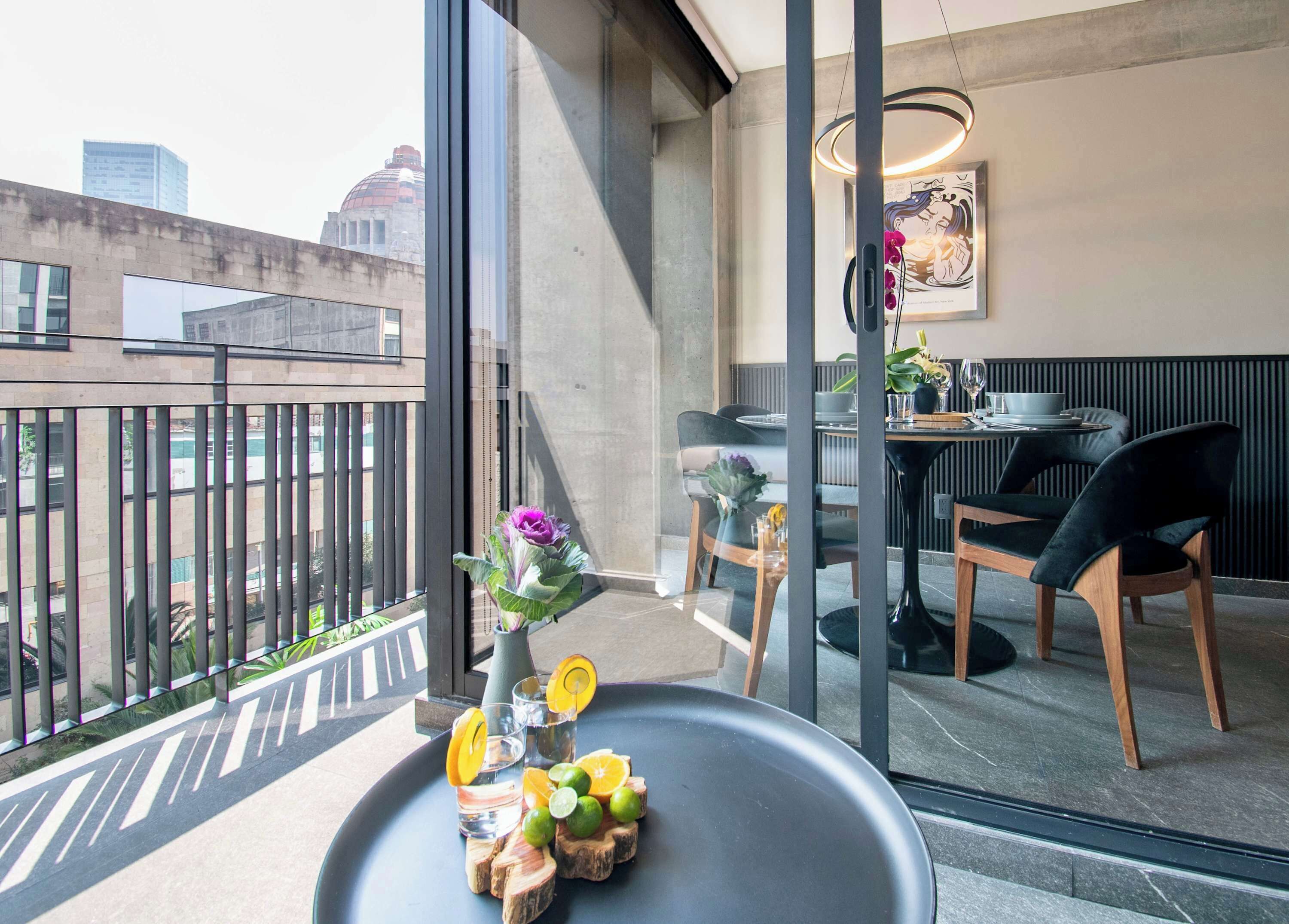 Un balcón con mesa, sillas, un florero y vista a la ciudad.