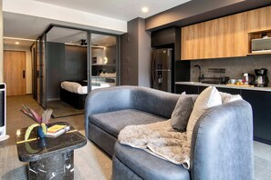 Ein modernes Wohnzimmer mit grauem Sofa, Couchtisch und Küchenbereich mit Kühlschrank und Mikrowelle.