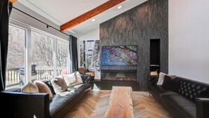 Una sala de estar moderna con chimenea, un televisor grande y un suelo de madera con diseño de espiga.