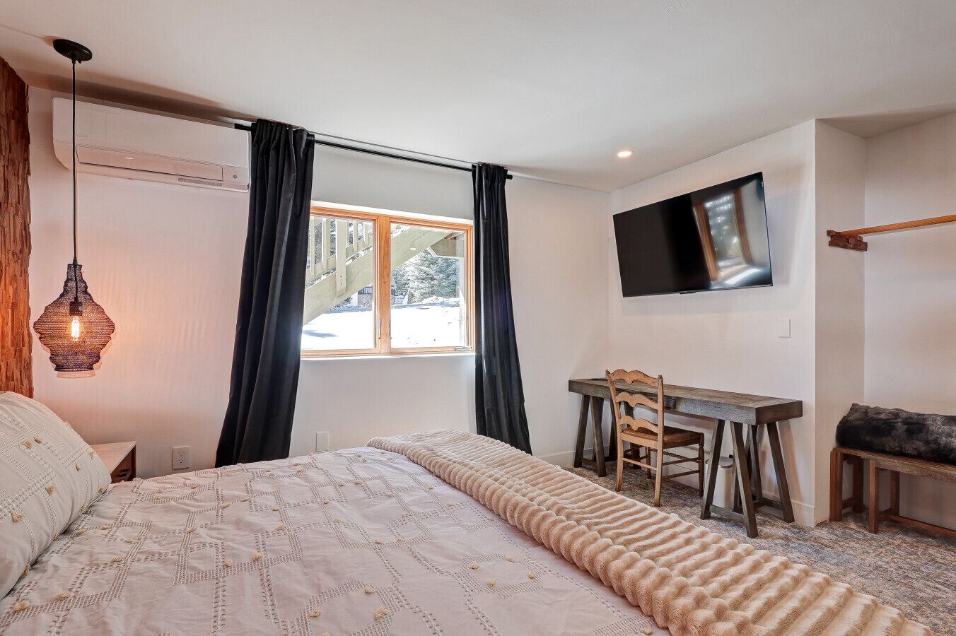 A bedroom with a bed, a desk, a chair, a TV, and a window with curtains.