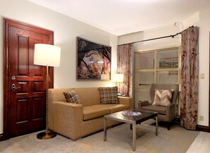 A living room with a sofa, armchair, coffee table, and a painting on the wall. - BC Lodge King Suite | Fireplace | Village Location (Beaver Creek)