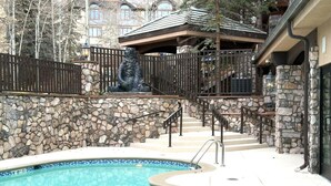 A pool area with stone walls, a metal fence, and a staircase leading to a building. - BC Lodge King Suite | Fireplace | Village Location (Beaver Creek)