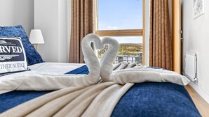 Quarto de hotel com cama, arranjo de toalha em formato de coração, vista para o exterior e um letreiro na parede.