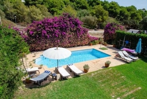 Ein rechteckiger Swimmingpool mit einem weißen Sonnenschirm, umgeben von Liegestühlen und einem kleinen Tisch.