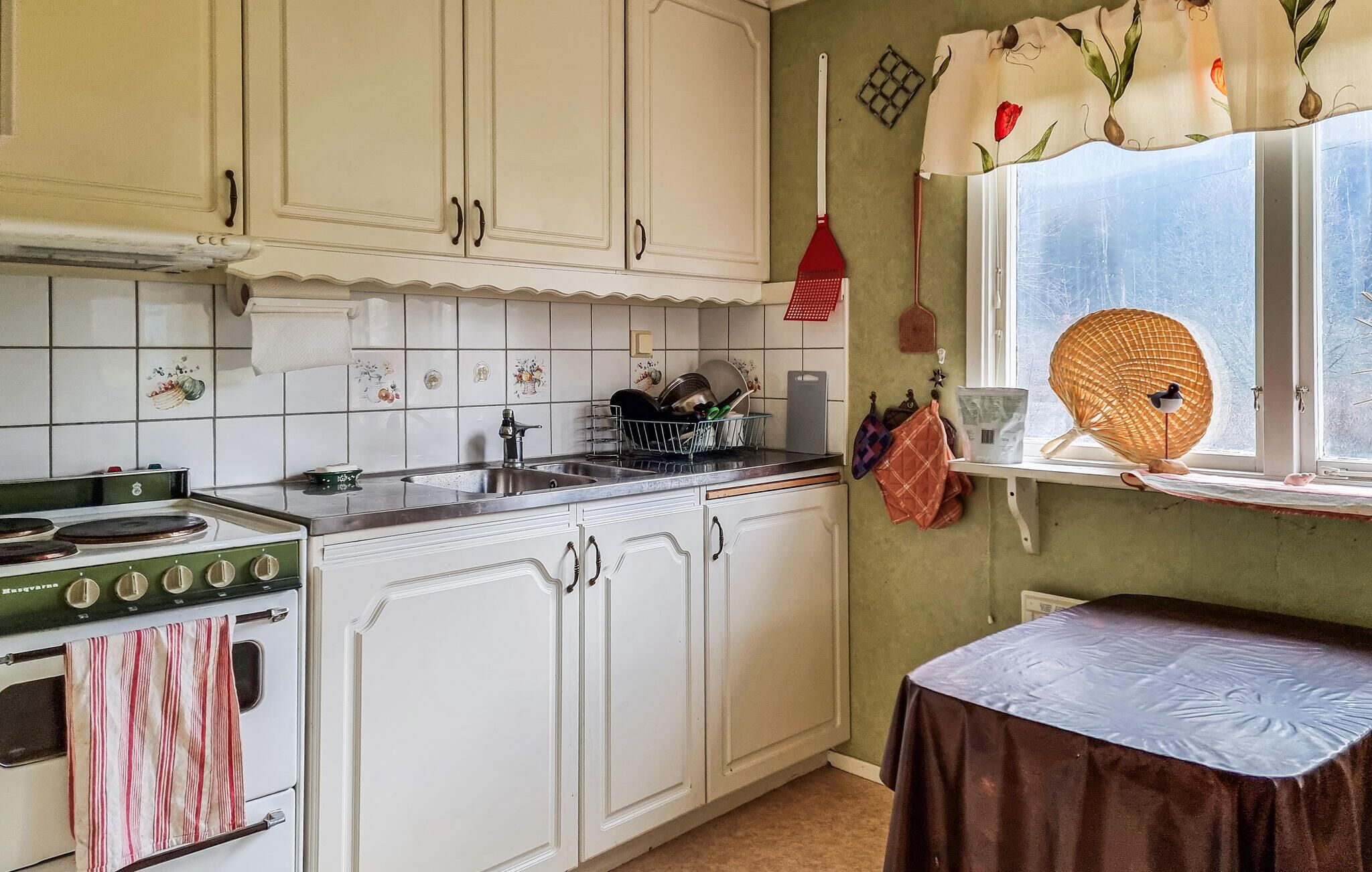 Cocina con armarios blancos, estufa y ventana con una cesta.