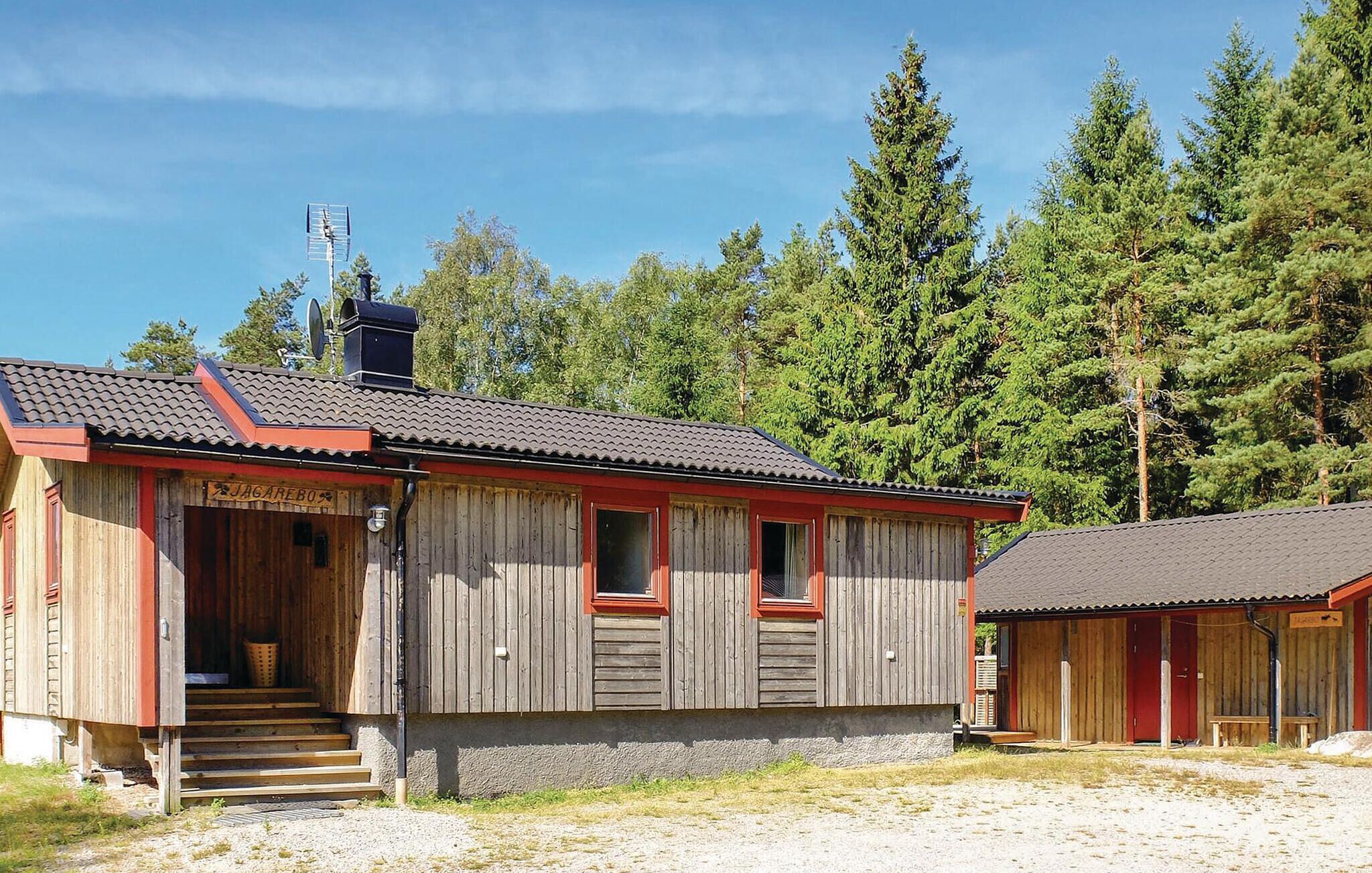 Punaisella katolla varustettu puinen mökki, jossa on savupiippu ja pieni kuisti, jonka portaat johtavat sisäänkäynnille.
