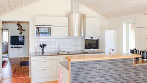 A modern kitchen with white cabinets, a stainless steel range hood, a built-in oven, and a large island with a tiled backsplash.