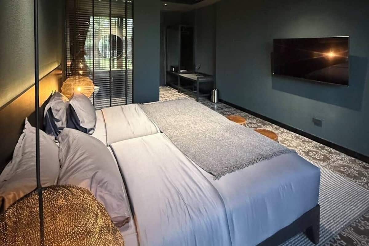 Un dormitorio moderno con una cama, lámparas de noche, un televisor y vistas al exterior.