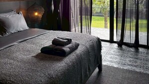 Ein Schlafzimmer mit einem großen Bett, transparenten Vorhängen und Blick auf Grünflächen.
