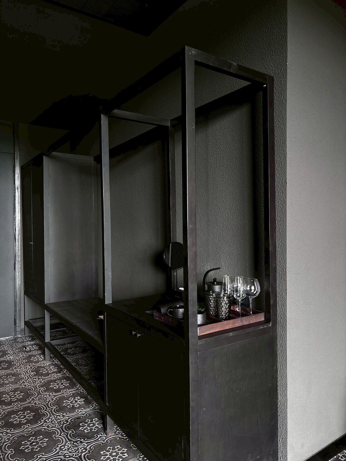 A room with a dark wooden bench, a small table with a kettle and glasses, and patterned flooring.