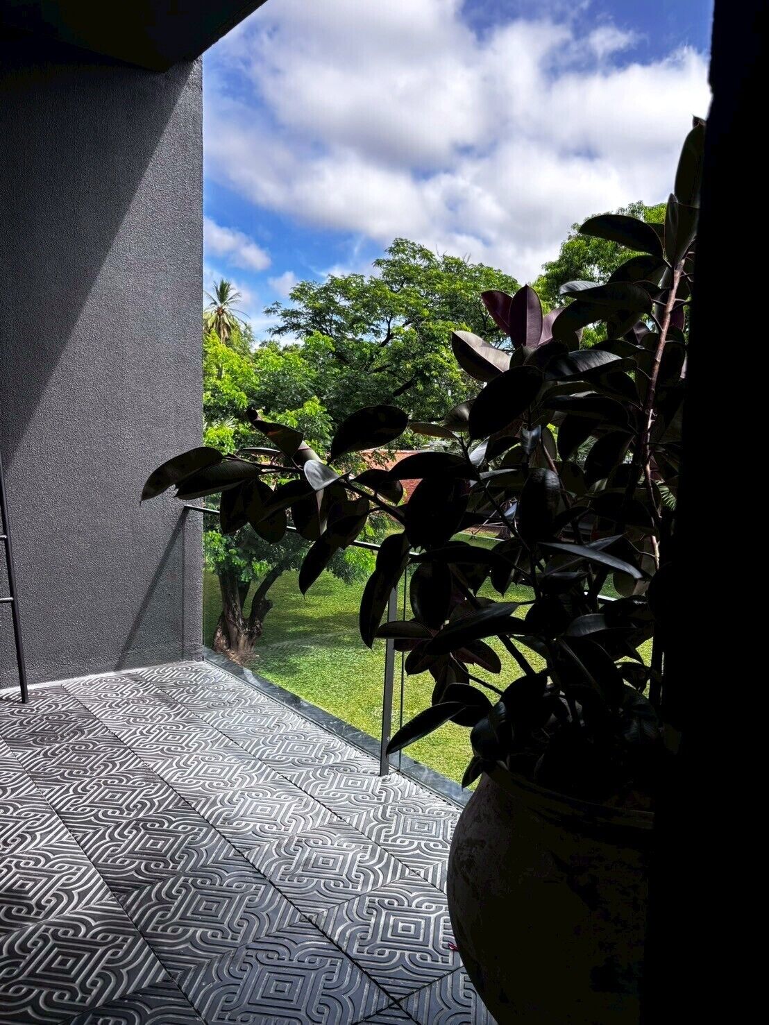 Un balcón con baldosas de diseño, una planta en maceta y vistas a un paisaje verde con árboles y cielo despejado.