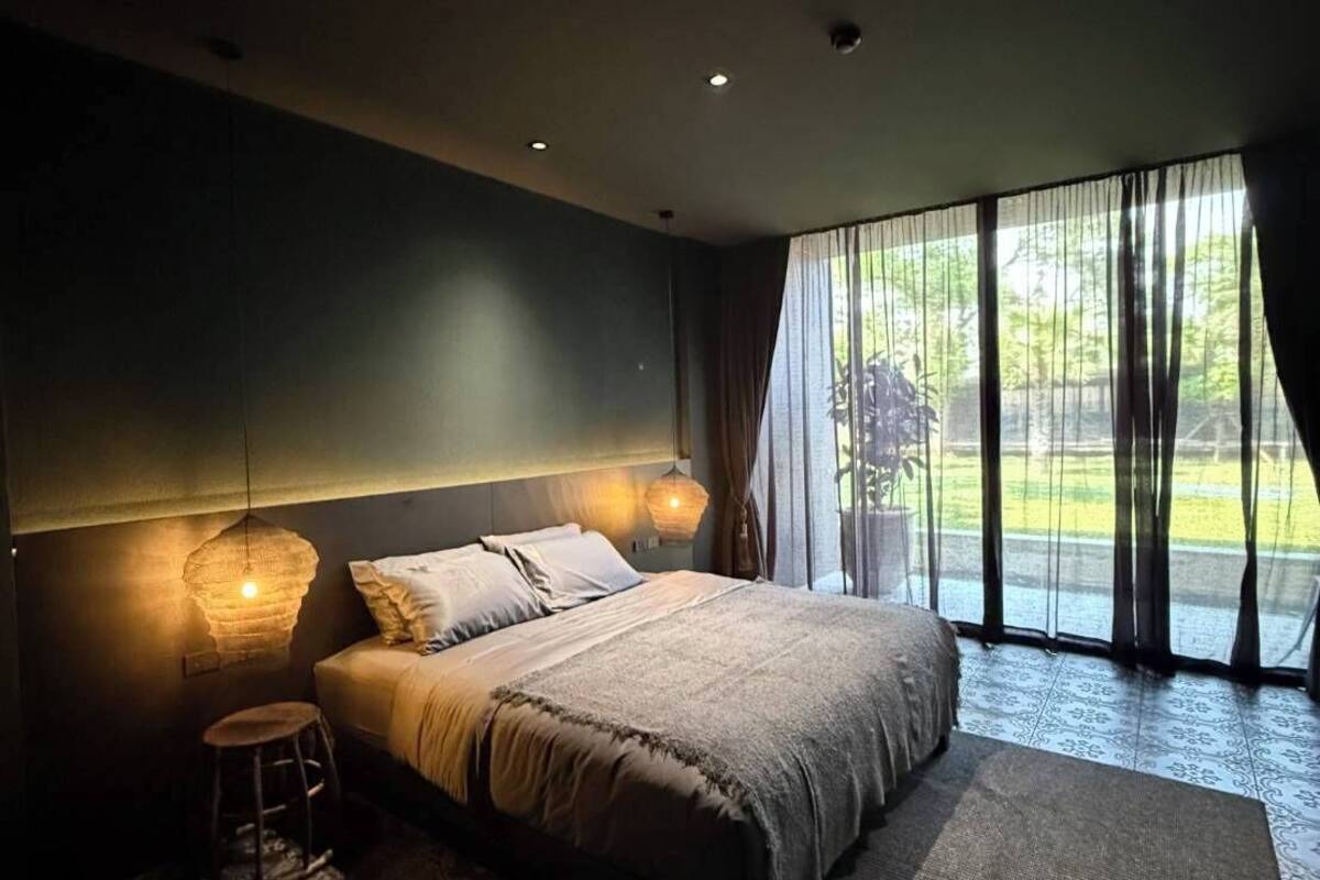 Un dormitorio moderno con una cama grande, un taburete pequeño y un ventanal con cortinas.
