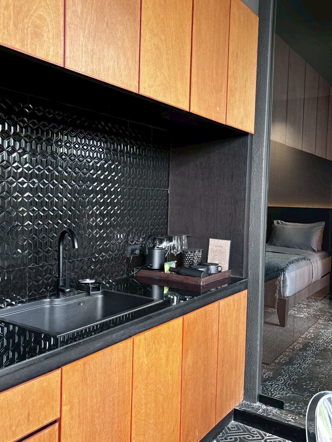 A compact kitchen with a black sink, wooden cabinets, and a patterned backsplash.