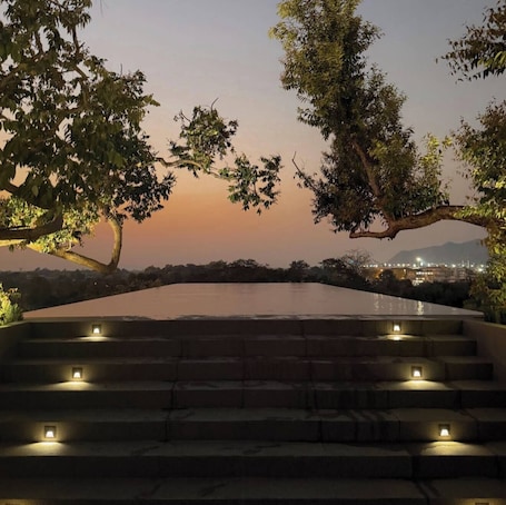 A pool with steps leading up to it, surrounded by trees and a cityscape in the background.