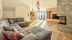 A modern living room with a sectional sofa, a stone fireplace, and a dining area with natural light. - Chalet in a beautiful setting (Albrechtice v Jizerskych horach)