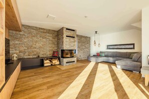 A modern living room with a stone wall, a fireplace, a gray sectional sofa, and a wooden floor.