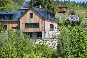 A modern wooden house with a sloped roof, large windows, and a stone foundation.