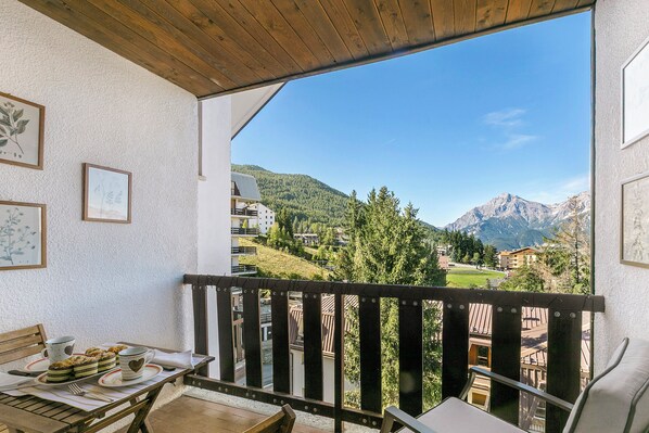 Ein Balkon mit Holzbalkon, ein Tisch mit einer Teller Essen und gerahmte Bilder an der Wand.