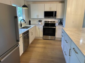 A modern kitchen with stainless steel appliances, white cabinetry, and a wooden floor. - The Velvet Antler- Rustic Lodge in Albany Texas (Albany)