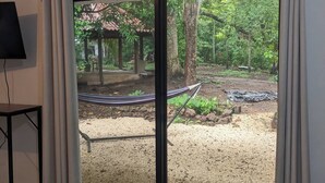 Une pièce dotée d’une grande porte-fenêtre coulissante donnant sur un espace extérieur aménagé avec un jardin, un hamac et une pergola.