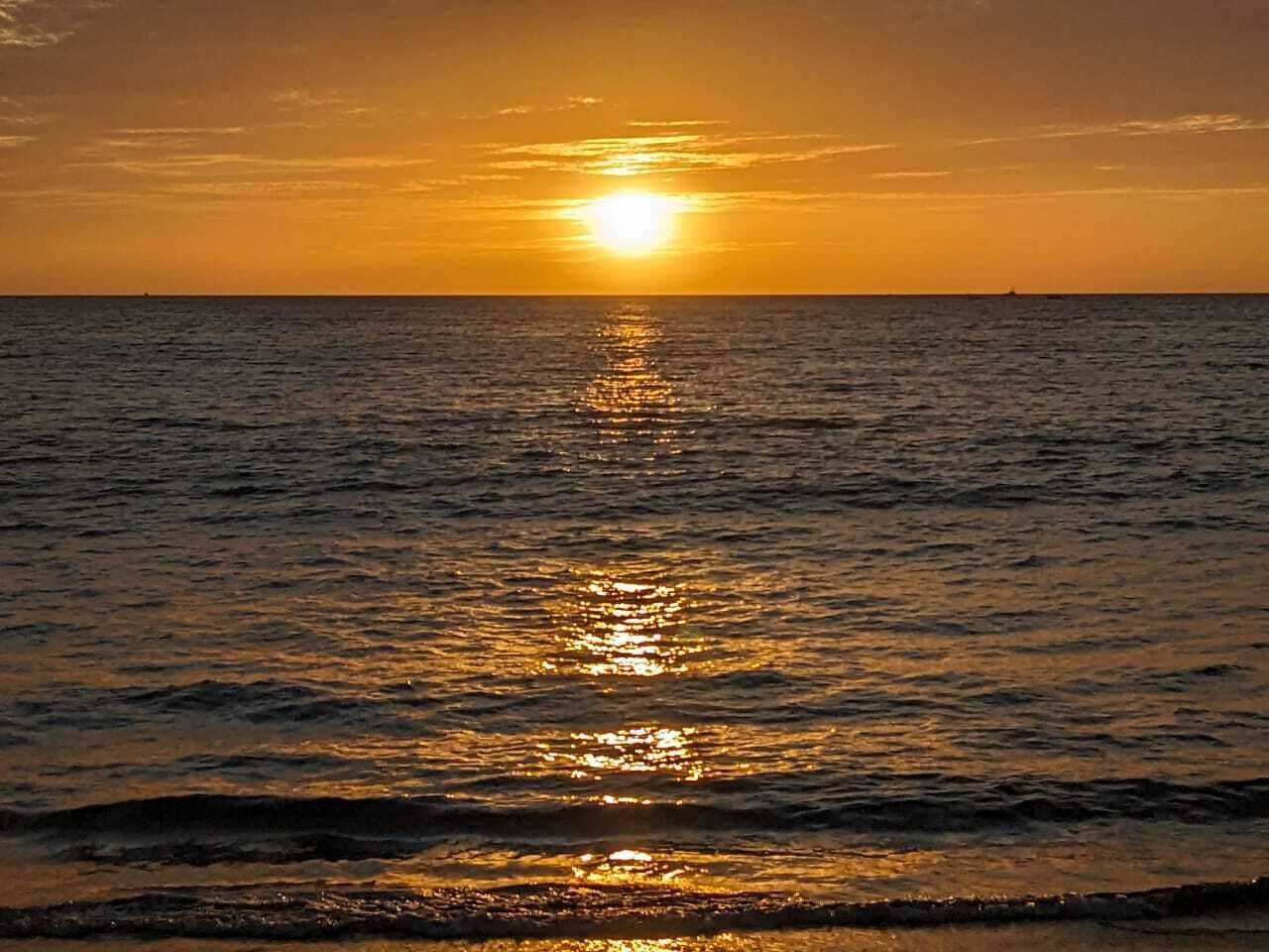 Um pôr do sol sobre o oceano, com águas calmas refletindo a luz do sol.