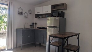 Une cuisine compacte avec des meubles gris, un réfrigérateur en acier inoxydable, un four à micro-ondes et une petite table accompagnée de deux tabourets.