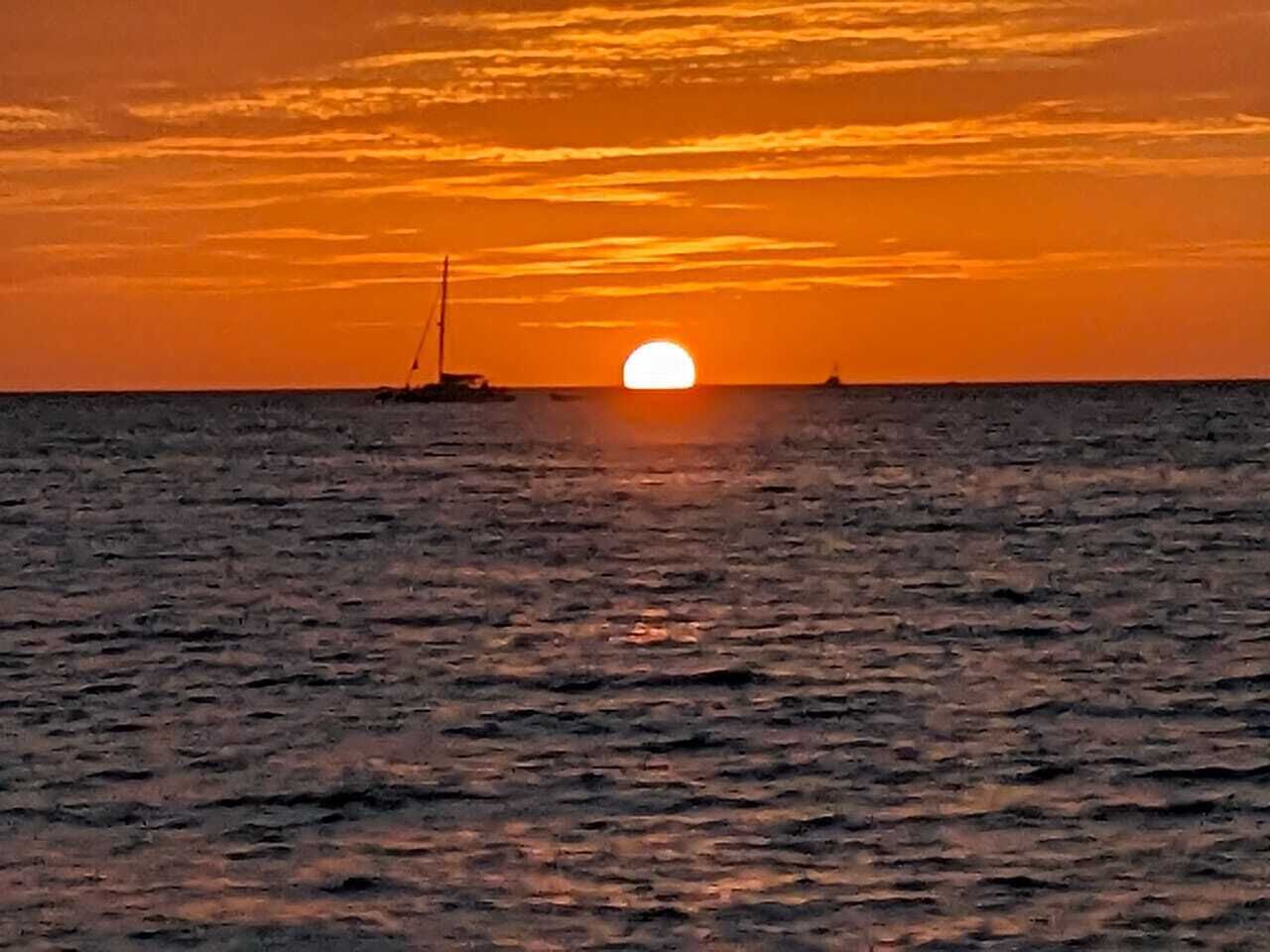 A sunset over the ocean with a sailboat in the distance.