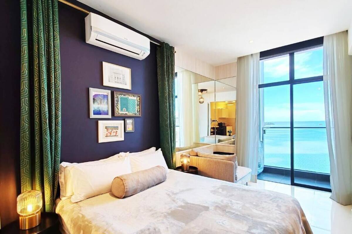 Een hotelkamer met een bed, nachtkastje, spiegel, raam met uitzicht op zee en ingelijste foto's aan de muur.
